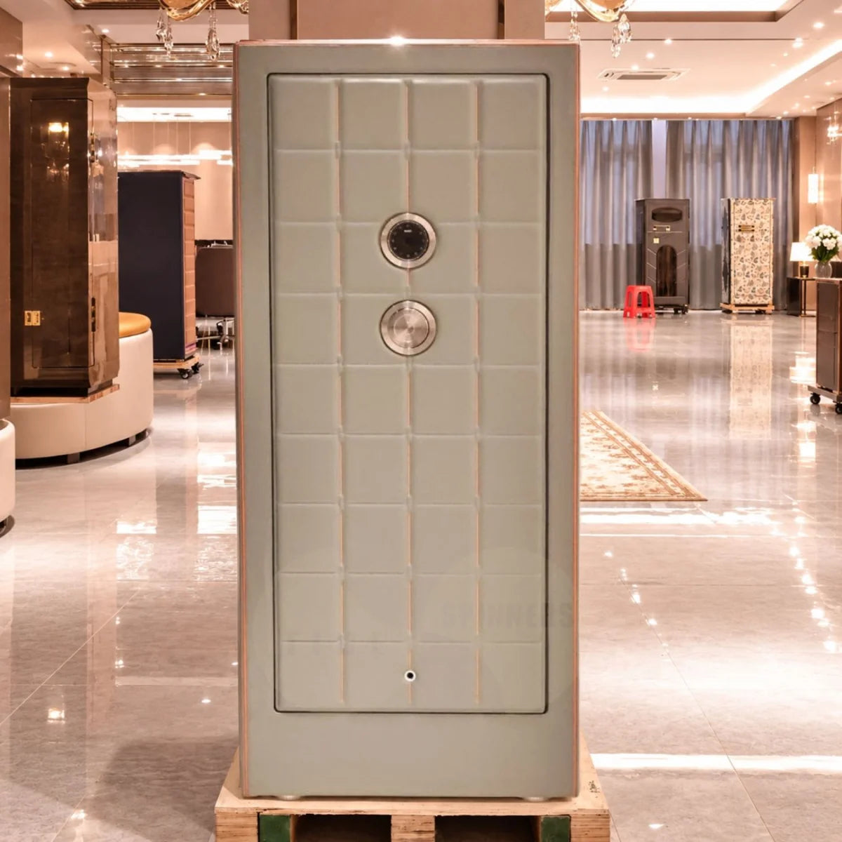 A tall, light gray security safe with a grid pattern and two circular dial locks, displayed on a wooden pallet in a polished hotel lobby.