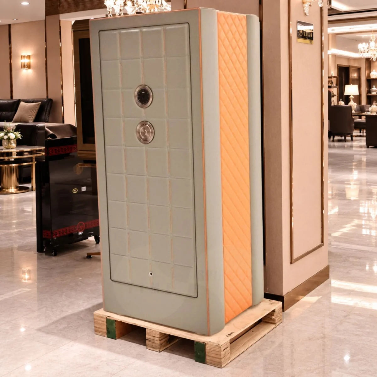A large safe on a wooden pallet in a luxury showroom. The safe features a light front door with a grid pattern, a textured orange quilted side panel, and two circular lock cylinders on the front.